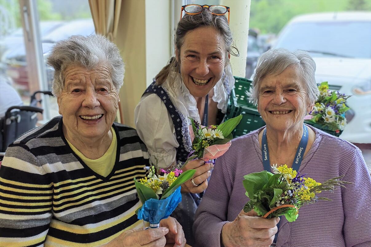 Die Mitarbeiterin Lydia Dörer überreicht den Bewohnerinnen Elisabeth Stramer und Edith Kren freudig die wunderschönen selbstgestalteten und -gepflückten Blumensträuße. 